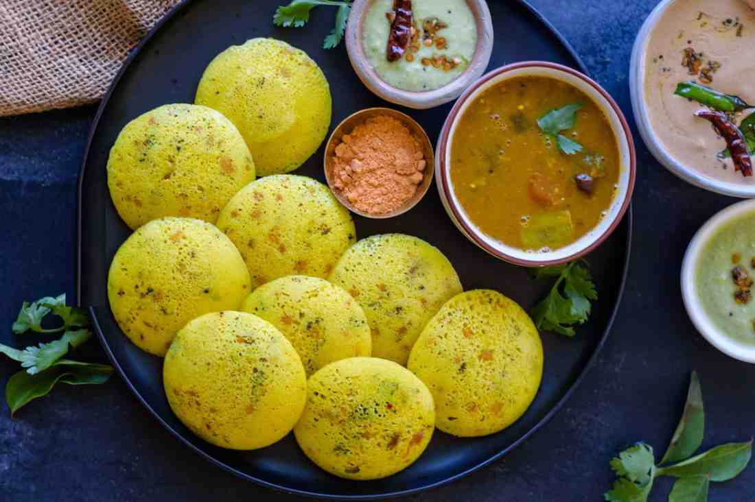 Kanchipuram Idli - A spiced version of idli with cumin, black pepper, and ginger, Why it’s healthy: More flavor, same health benefits as plain idli, rigin - Tamil Nadu temples, Spiced idlis stacked in banana leaf bowls